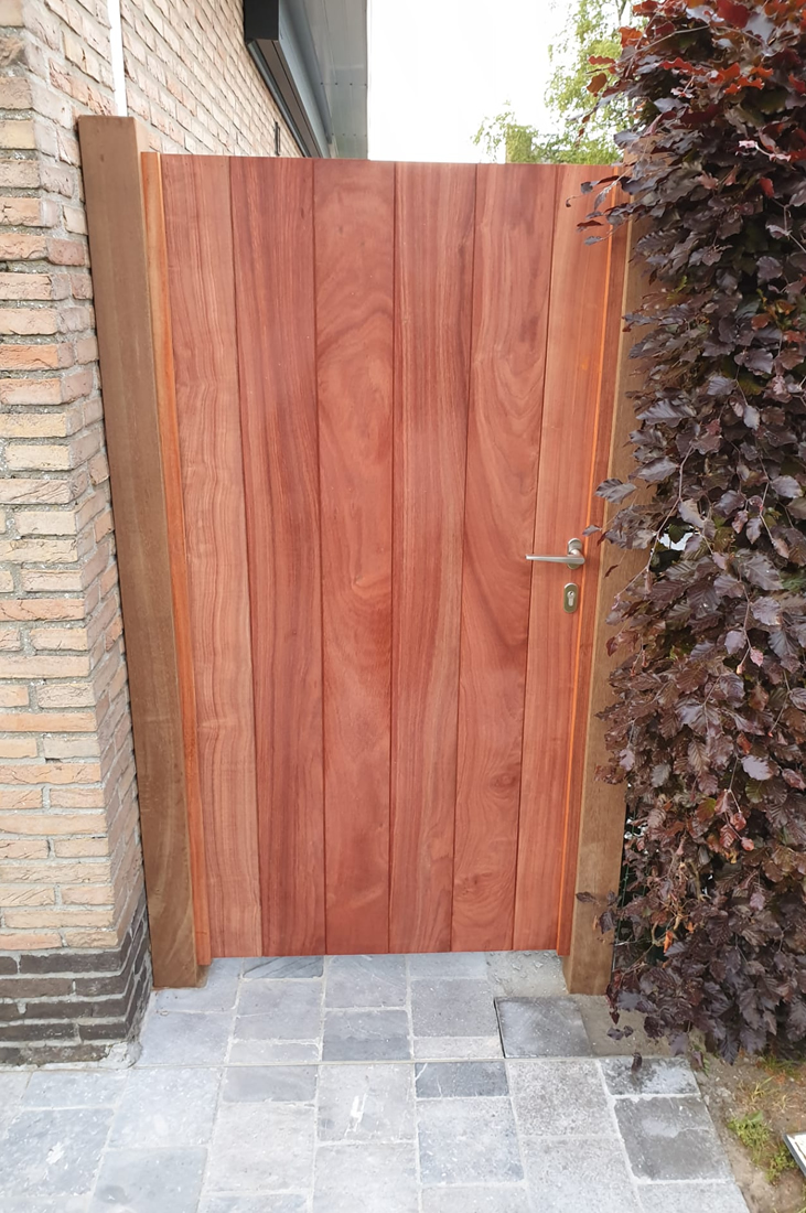 Houten deur als ingang tuin via pad naast gevel huis voor klant uit Oost Vlaanderen